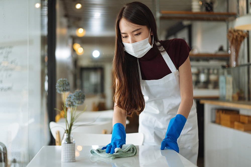 Waitress wearing face mask cleaning table in coffee shop restaurant